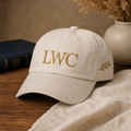 LWC Walk by Faith embroidered dad cap front close-up in stone with enlarged LWC monogram and clean side olive branch.
